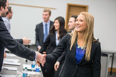 Several students wearing suits shake hands with adults across a table.